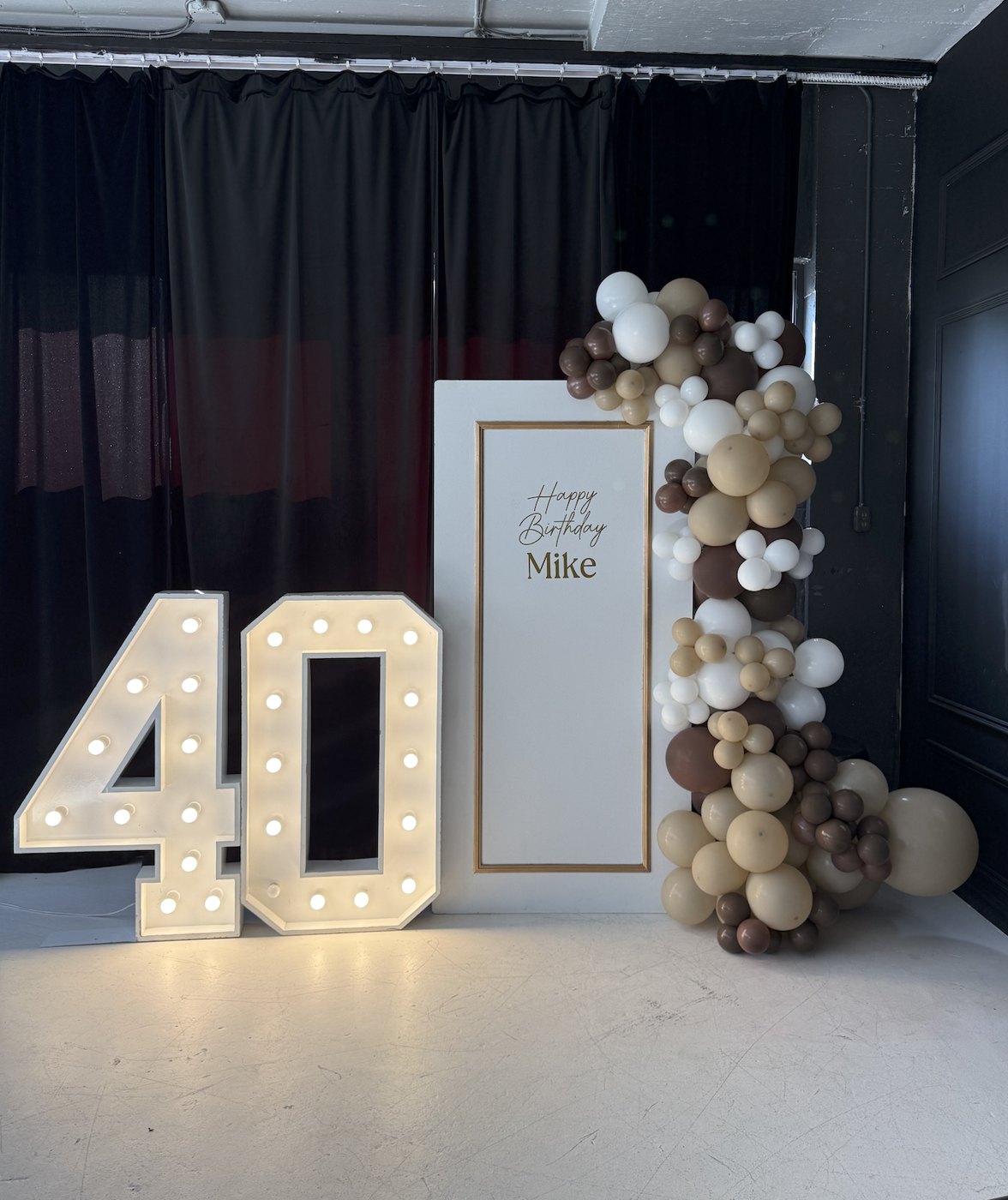 Backdrop d’anniversaire Nad’CO : panneau blanc et or, chiffres lumineux 40 et ballons nude, chocolat et blanc