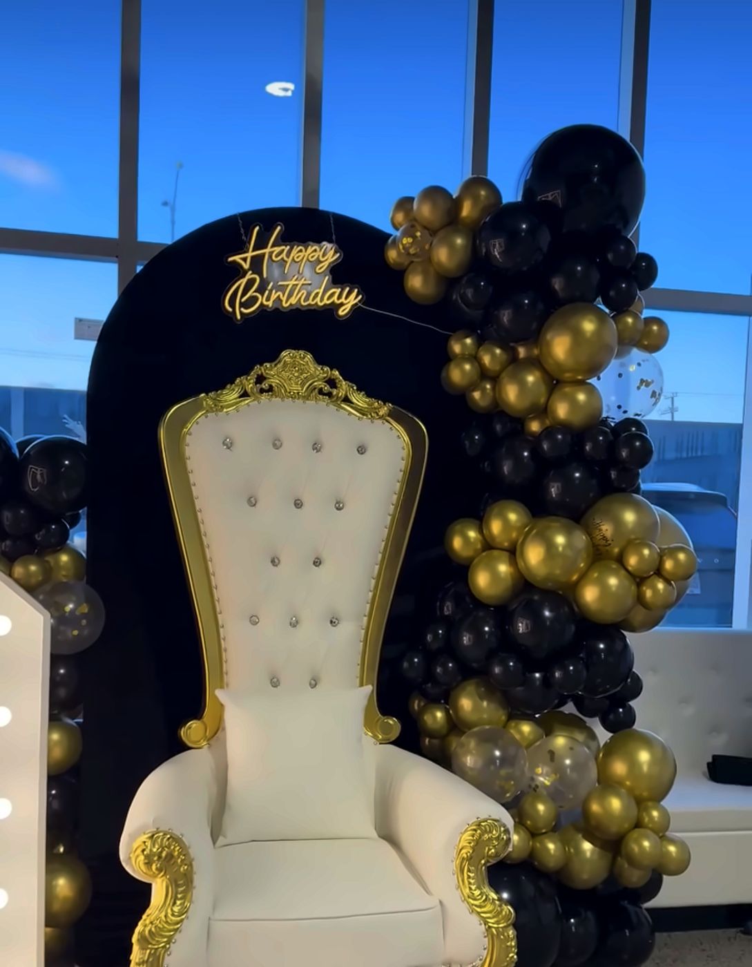 Chaise trône blanche devant une arche noire et ballons dorés
